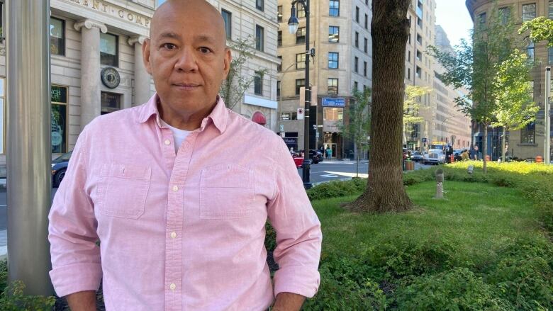 bald Asian man wearing a pink button-up shirt and blue jeans with a brown belt and watch standing outside on a summer day