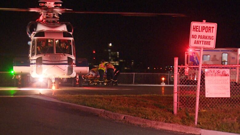 A helicopter sits on a tarmac as an injured worker is wheeled to a waiting ambulance.