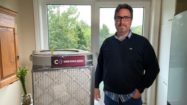 Olivier Drouin standing next to a filter box with the COVID coles Qubec logo on it.