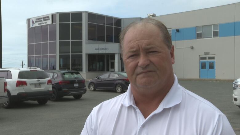 A man in a white shirt stands in front of a glass union building.