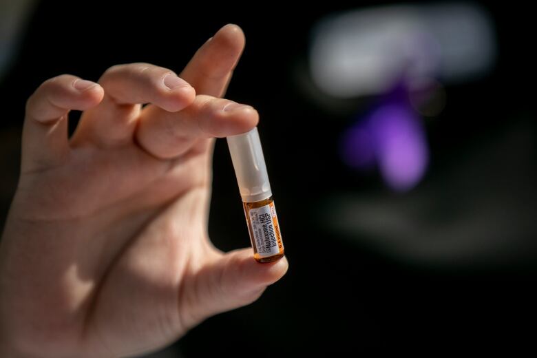 A hand holds a small tube marked with the word naloxone.