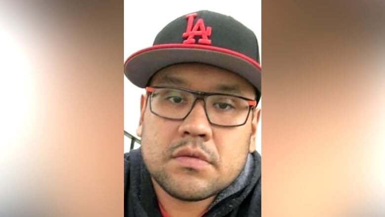 Man wearing glasses, and black and red hat poses for a selfie.