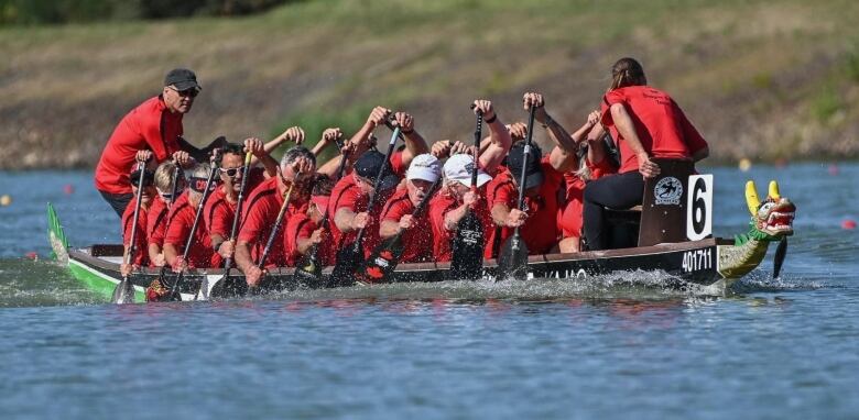 People wearing red shirts paddle a boat in the water.