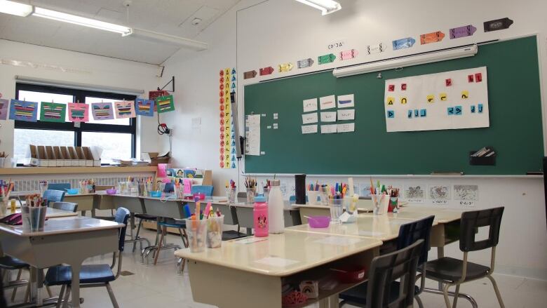 An empty classroom featuring small chairs, children's art and Inuktut syllabics on the chalkboard.