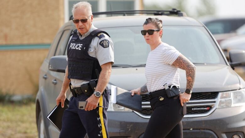 A uniformed RCMP officer and a plain clothes investigator walk past a vehicle in the aftermath of a stabbing spree on James Smith Cree Nation in September 2022.