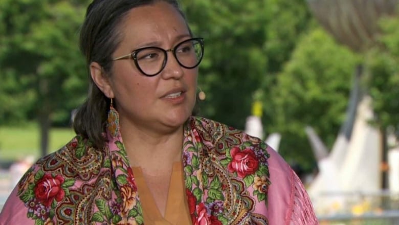 A Cree woman with a floral scarf looks to the side in a close-up photo.