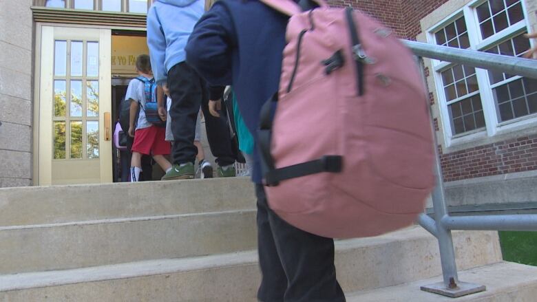 Students wearing backpacks walk up the stairs into a school.