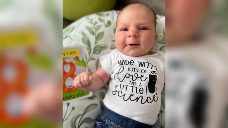 A baby wears a shirt that says Made with lots of love and a little science.