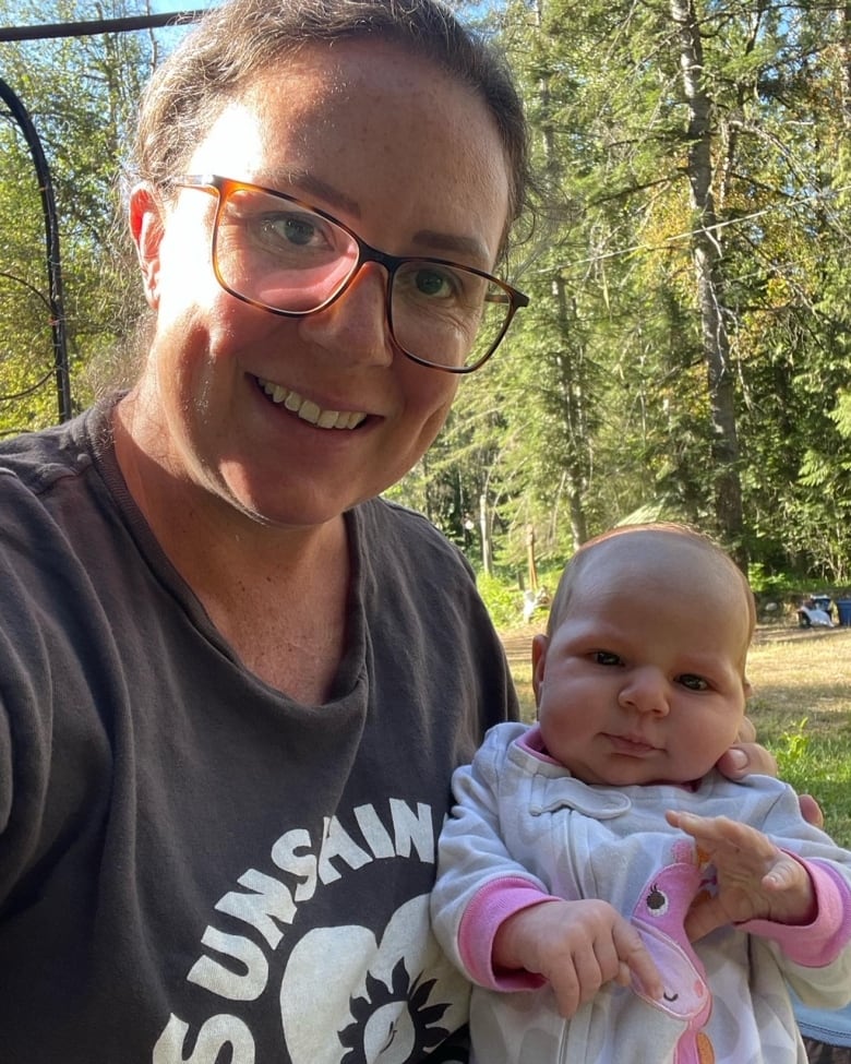 A woman holds a baby in her arms while sitting in a forest.