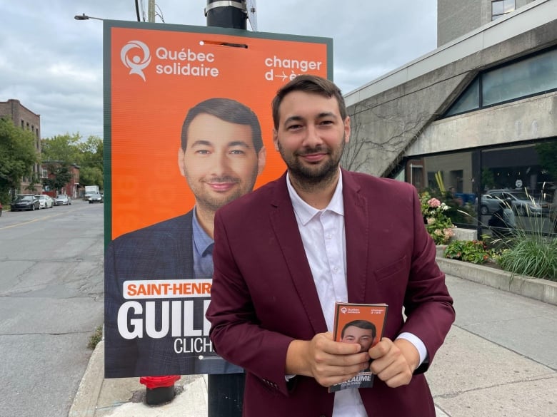 A man stands in front of an election campaign sign.