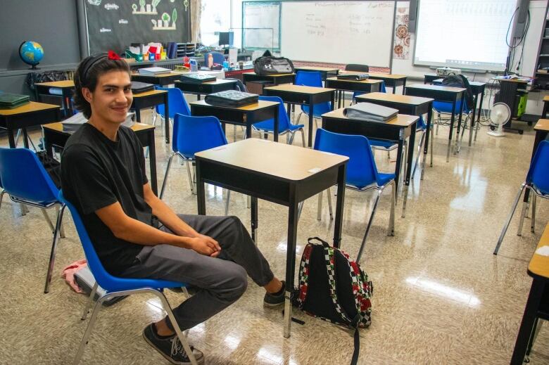 A young man sits at a desk in a classroom.