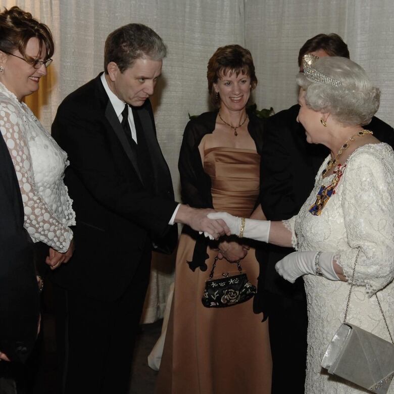 A man in a suit shakes hands with Queen Elizabeth 