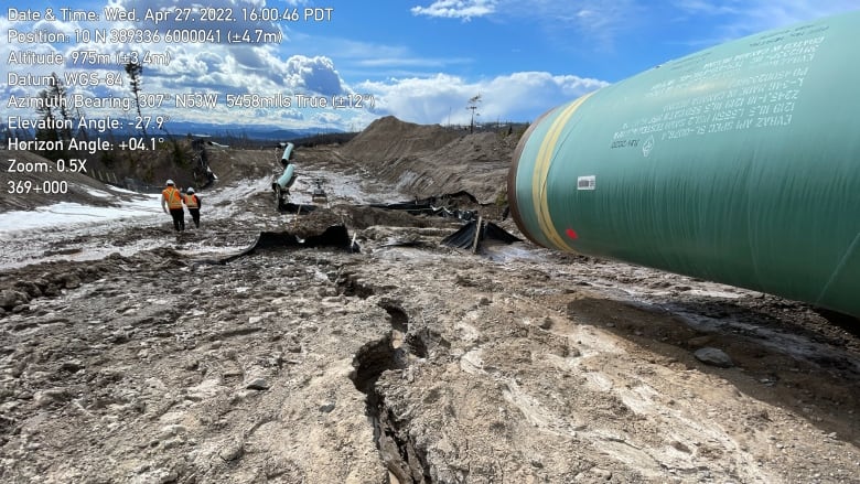 Cracks are seen in dry soil with a green pipe to the right of it.