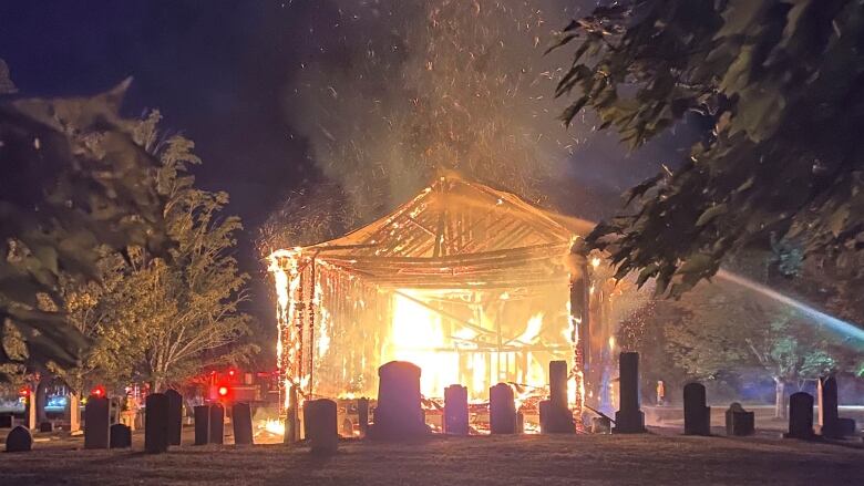 a bright inferno consumes the shell of a wooden church creating silhouettes of gravestones.