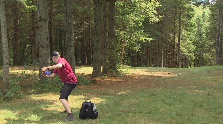 A disc golf player holds a frisbee standing in a wooded area