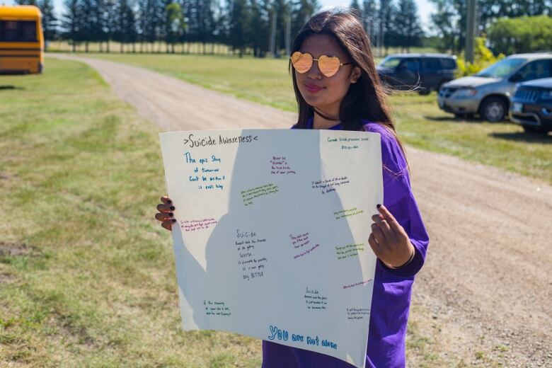 A young girl wearing heart shaped sunglasses holds a sign promoting world suicide prevention day.