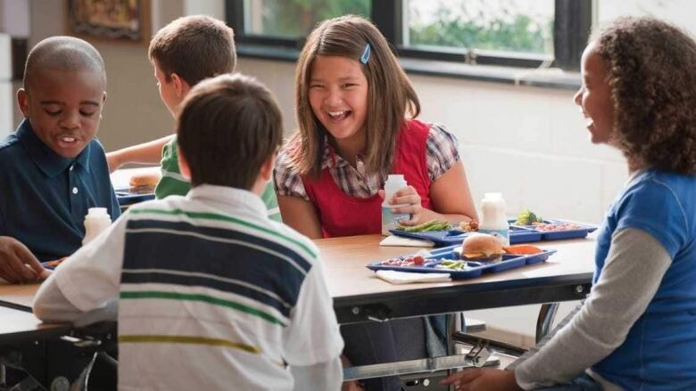 A number of children laugh at a lunch table.