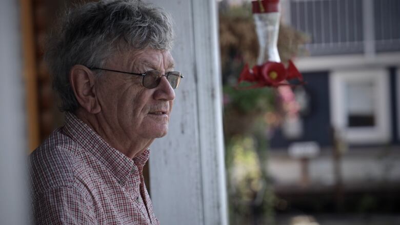 A man looks pensive as he stares beyond the camera. He is wearing shaded glasses and has grey hair.