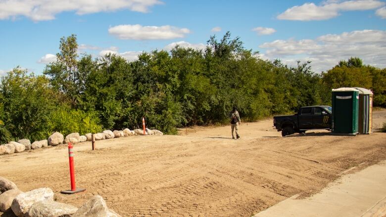 A person walks through a construction site with rocks and a Porta Potty.