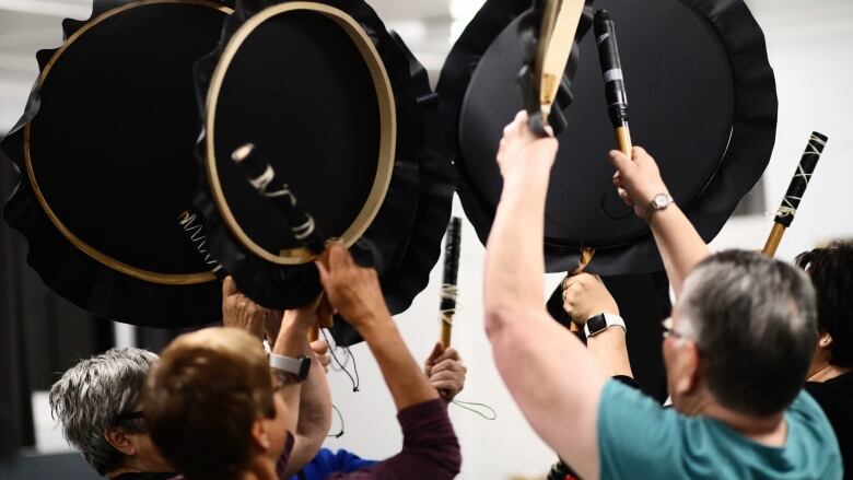 Six black drums are lifted up into the air by Elders and adults in Cartwright. 