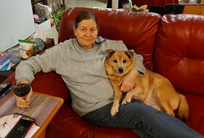 A portrait of woman sitting on a couch with a dog in her lap and a glass of wine in her hand.