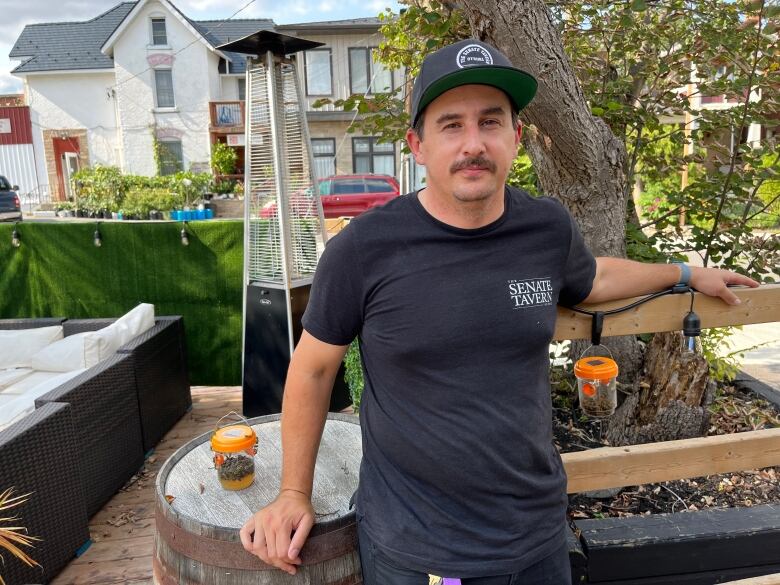 Grant Marley posing on the patio at the Senate Tavern with two homemade wasp traps on either side of him in a clear container with orange lid. 