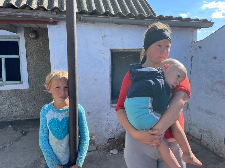 A woman in a red t-shirt holds a young boy in her arms as a young girl wearing a sweater with a blue heart looks on. 