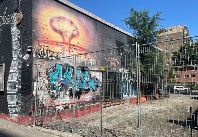 A fenced off building with a atomic bomb mural defaced by competing graffiti. 