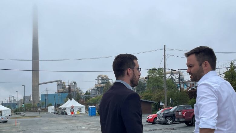 Two men in the foreground, a smokestack in the background.