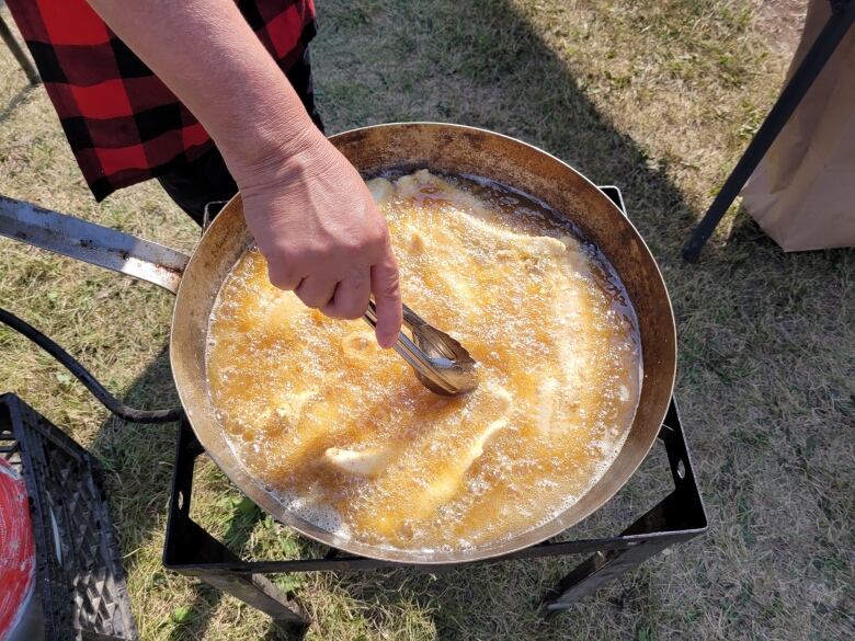 A person dips a pair of tongs into a vat of oil to grab a fish being fried.