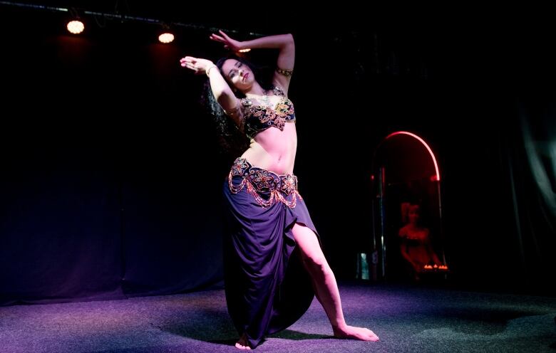 Oksana Makarenko performs a belly dance routine on stage. A purple stage line is shining on her.