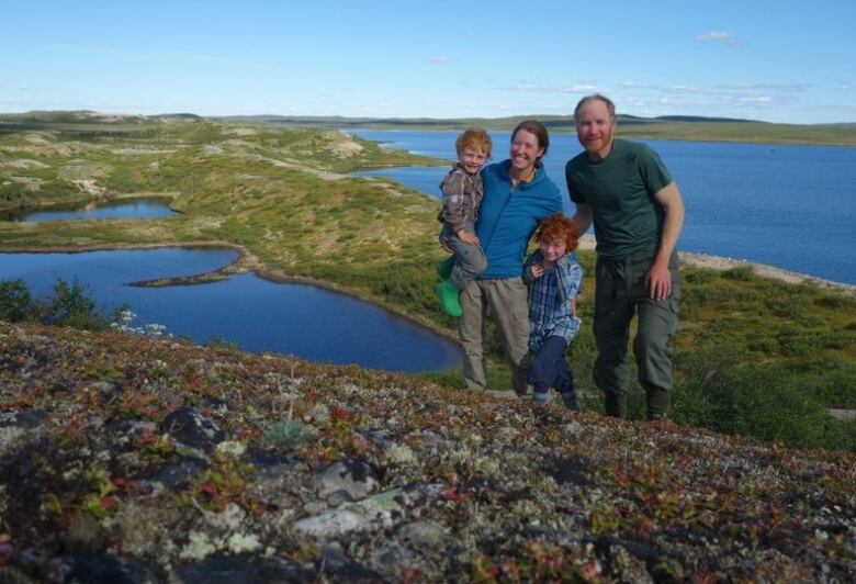 A man, woman and two young boys pose on a hillside with tundra and lakes visible behind them.