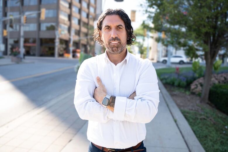 A man in a white shirt stands on a downtown Windsor sidewalk with his arms crossed