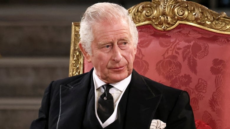 An older man sits in tall-backed chair with gold-painted trim. 