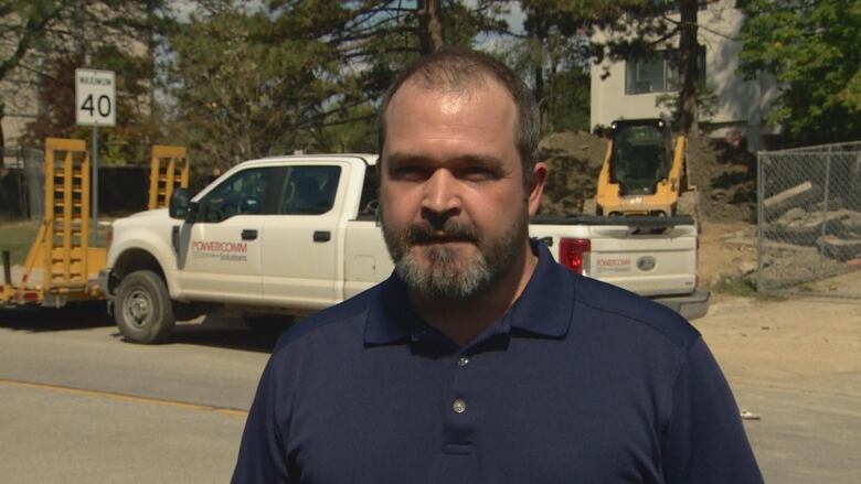 Mike Reid stands in front of the building he lives in, with construction vehicles in the background.