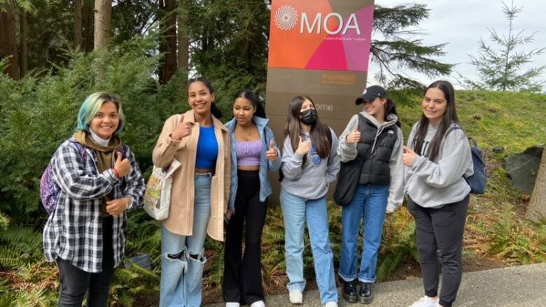 A group of young girls pose in front of the Museum of Anthropology sign.