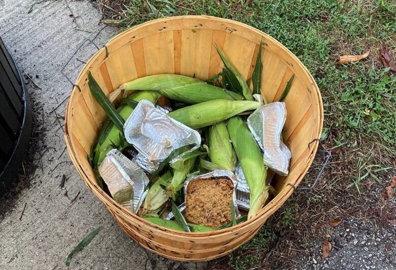 A bowl of corn and leftover food in a basket outside.