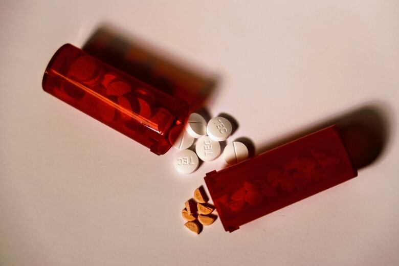 Orange pill bottles containing prescription drugs spill onto a white table.