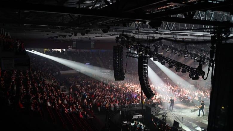 A musician performs in front of a large arena audience.