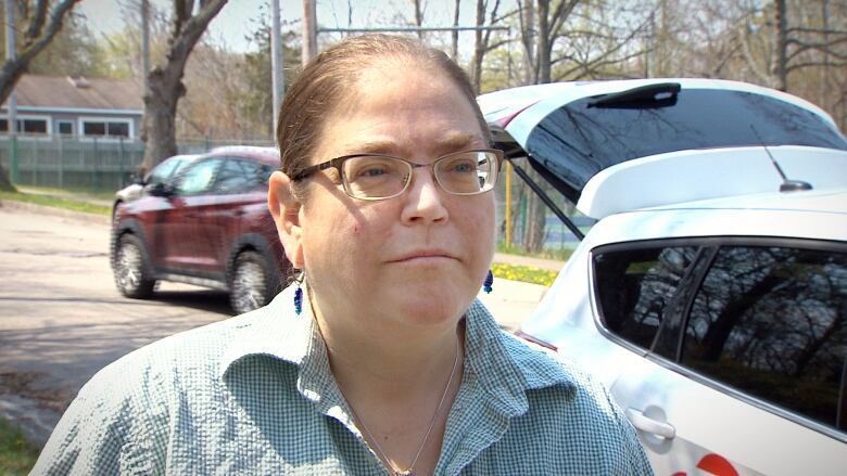 Woman with hair pulled back and wearing glasses and a checked shirt looks to the right.