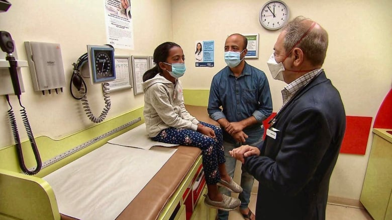 A doctor examines a young patient as her father looks on