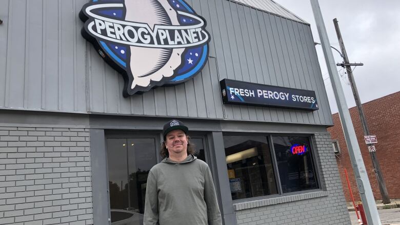 A man stands in front of a store with a sign saying 