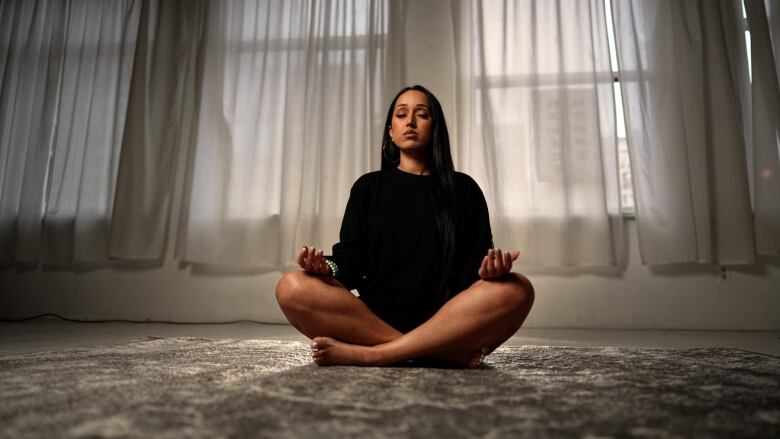 Summan sits cross-legged on the floor, with her hands in a yoga mudra (posture).