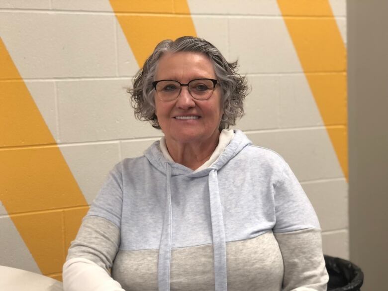 A woman sits before a white and yellow wall.