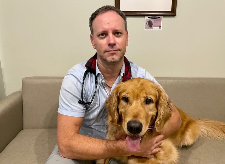 Veterinarian Ian Cameron in his office holding a golden retriever in his arms. 