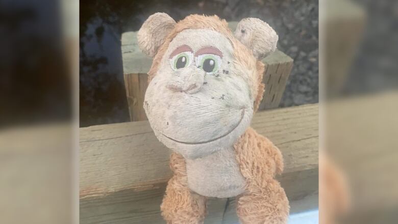 A dirty stuff monkey toy is resting on the wood of a bridge railing