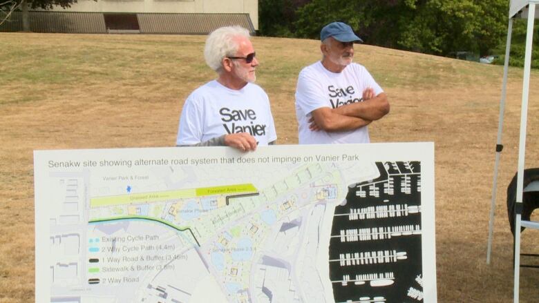 Two old men stand near a sign with the proposed site plans for the Senw development.