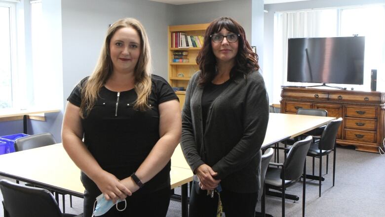 Two women stand in a large, empty board room.