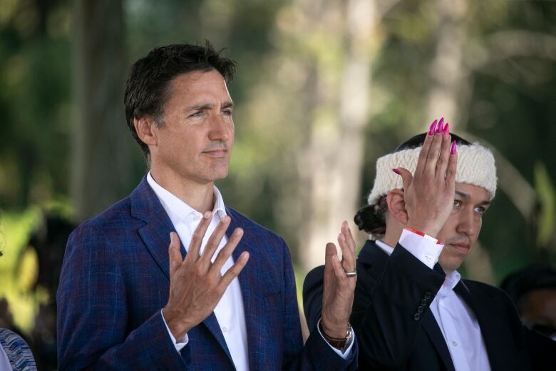 Justin Trudeau and Khelsilem hold their hands up in a Squamish gesture meant to honour the lands.