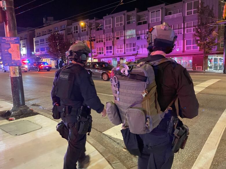 Two police officers wearing tactical gear are shown from behind as they cross a Vancouver street.